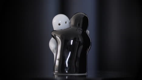 Black-and-white-hugging-Porcelain-figurines-rotating-on-reflective-surface,-black-background
