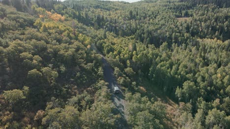 A-car-driving-along-a-mountain-road-through-the-forest---tilt-up-aerial-view-to-reveal-the-autumn-wilderness-landscape