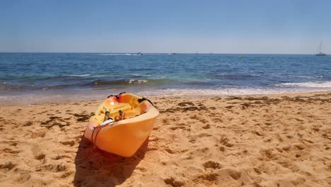 Slow-motion-shot-of-waves-lapping-on-a-warm-sunny-sandy-beach-behind-a-modern-yellow-open-kayak
