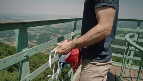 Man-reached-top-of-lookout-tower-and-taking-a-slovenian-flag-out-of-his-backpack-and-tie-it-up-on-the-fence