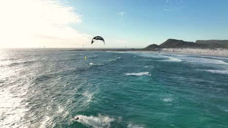 Drone-Siguiendo-A-Un-Kitesurfista-Saltando-Fuera-Del-Agua-En-Un-Acantilado-Brumoso-Cerca-De-Ciudad-Del-Cabo,-Sudáfrica