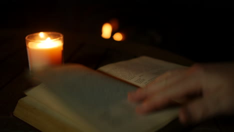 Ein-Mann,-Der-Ein-Altes-Antikes-Buch-An-Einem-Gemütlichen-Feuer-Liest-Und-Von-Kerzenlicht-Beleuchtet-Wird
