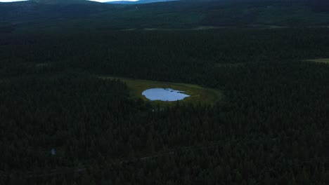 Vuelo-Aéreo-Sobre-Las-Copas-De-Los-Pinos-Y-Un-Pequeño-Lago-En-Suecia,-Aurora-Camp-Kurravaara