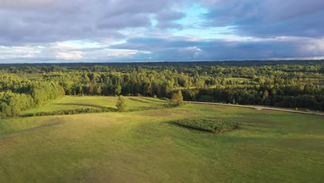 Exuberantes-Campos-Verdes-Y-árboles-Con-Un-Lago-Tranquilo-Detrás-En-La-Puesta-De-Sol-De-La-Hora-Dorada-En-Strante,-Letonia