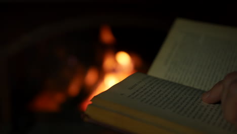 A-man-reading-a-book-close-to-an-open-fire-in-a-fireplace-in-a-dark-room