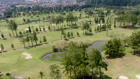 Exotic-golf-course-with-palm-trees-and-water-pond-in-Indonesia,-aerial-view