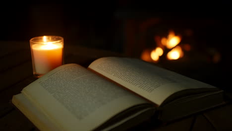 Ein-Altes-Antikes-Buch,-Das-Auf-Einem-Von-Kerzenlicht-Beleuchteten-Tisch-Mit-Offenem-Feuer-Und-Kamin-In-Einem-Dunklen-Raum-Geöffnet-Ist