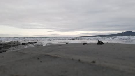 Blick-Vom-Erdgeschoss-Auf-Kleine-Wellen,-Die-Sich-Einem-Strand-Mit-Dunklem-Sand-Auf-Der-Nordinsel-Neuseelands-Nähern