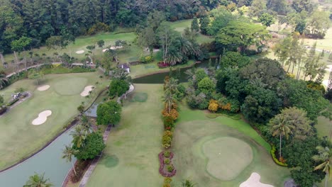 Tropical-golf-course-with-water-pond-and-palm-trees,-aerial-fly-above-view