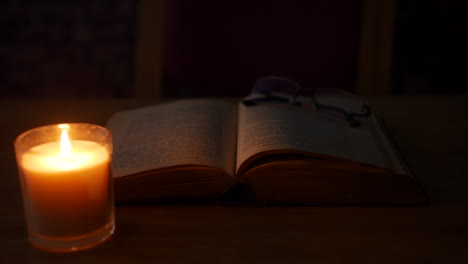 Eine-Brille-Auf-Einem-Alten-Antiken-Buch-In-Einem-Dunklen-Raum,-Der-Von-Kerzenlicht-Beleuchtet-Wird