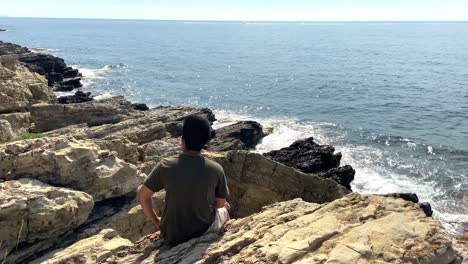 Young-Man-Sitting-On-The-Rocks-Enjoying-The-View-Of-Ocean-At-Summer-In-Saint-Jean-Cap-Ferrat,-France