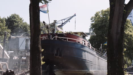 An-old-moored-houseboat-flying-the-dutch-flag-with-steamy-smoke-on-a-summery-day