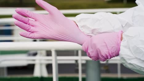 Man-wearing-white-protective-suit,-putting-on-pink-latex-gloves,-standing-on-a-boat