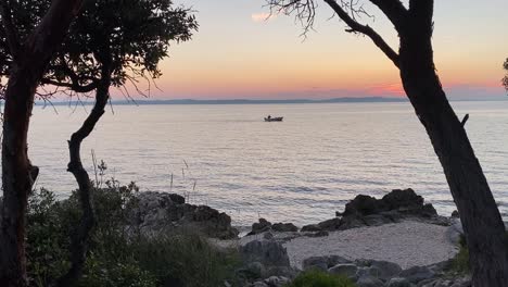 Fisherman-sailing-at-dusk,-view-between-the-trees,-hand-shot,-Croatia