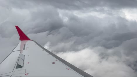 Side-view-of-a-medium-jet-plane-crossing-a-turbulent-sky-plenty-of-stormy-clouds-with-the-airbrakes-deployed-and-a-red-winlet