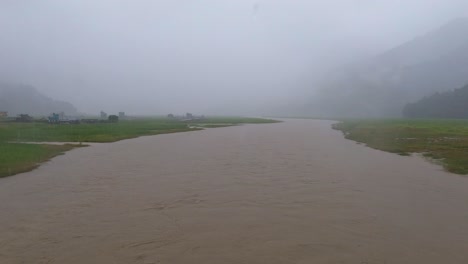 Parado-En-Un-Puente-Bajo-Una-Fuerte-Lluvia-Mirando-El-Río-Inundado-Durante-El-Monzón-En-Nepal
