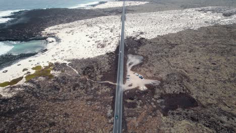 aerial-shot-of-long-lonely-road,-covered-by-sand,-next-to-the-ocean-nad-rocky-beach
