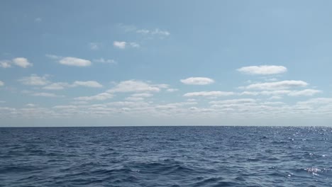 Peaceful-panorama-view-of-blue-open-ocean-with-sun-reflection-on-calm-ripple-waves-and-small-clouds-in-the-background-on-a-beautiful-sunny-day
