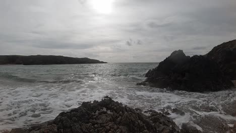 Calming-slow-motion-foaming-ocean-waves-crashing-against-rocky-Welsh-coastline-at-sunrise