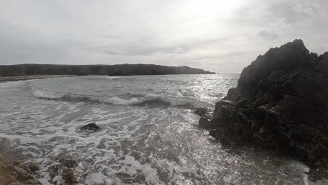 Slow-motion-calming-foaming-ocean-waves-breaking-against-rugged-Welsh-shoreline-at-sunrise