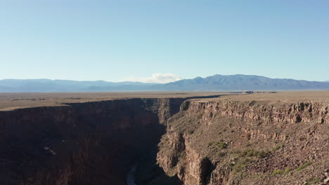 Aerial-of-desert-river-gorge-with-large-wildfire-burning-in-distant-mountains