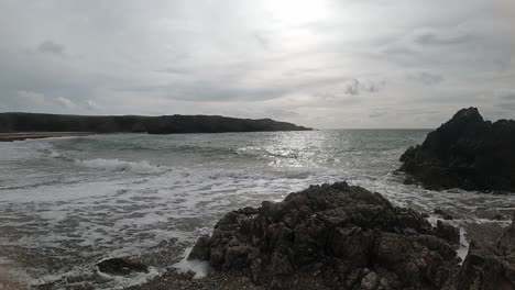 Slow-motion-shimmering-ocean-waves-breaking-against-rugged-Welsh-seashore-at-sunrise