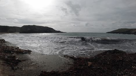 Peaceful-slow-motion-foaming-ocean-tide-breaking-against-rugged-Welsh-sand-coastline-at-sunrise