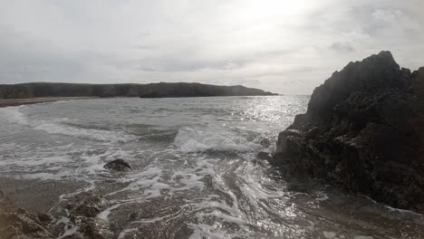 Calming-slow-motion-foaming-ocean-waves-crashing-against-rugged-Welsh-coastline-at-sunrise