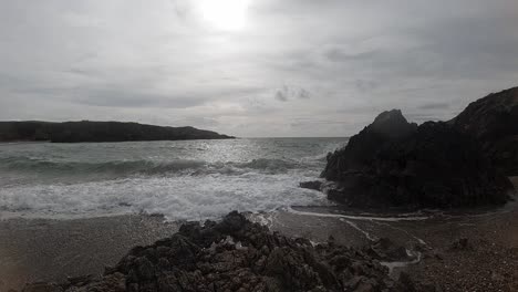 Peaceful-slow-motion-foaming-ocean-waves-breaking-against-rugged-Welsh-coastline-at-sunrise