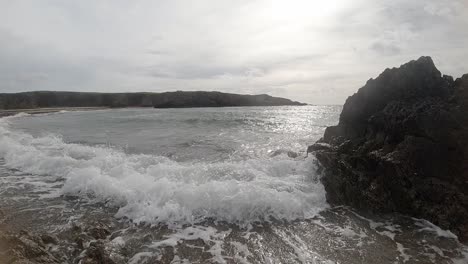 Slow-motion-foaming-shimmering-ocean-waves-crashing-against-rocky-Welsh-coastline-at-sunrise