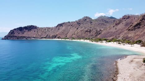 Stunning-view-of-turquoise-ocean-with-crystal-clear-water,-white-sandy-beach-and-rugged-hills-and-mountains-on-the-remote-tropical-island-of-Timor-Leste,-Southeast-Asia,-aerial-drone-of-Dili-landscape