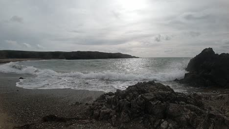 Slow-motion-quiet-foaming-ocean-waves-crashing-against-rocky-Welsh-sandy-coastline-at-sunrise