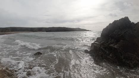 Peaceful-slow-motion-foaming-ocean-waves-crashing-against-rugged-Welsh-coastline-at-sunrise