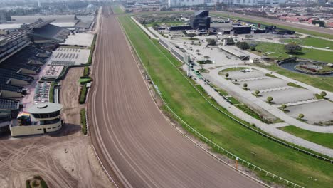 Drone-video-of-a-horse-dirt-race-track,-with-a-green-grassy-area-in-the-middle-also-with-buildings