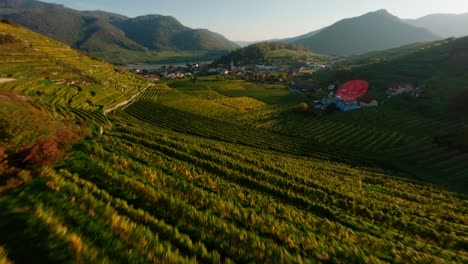 High-energy-FPV-shot-flying-throug-the-red-gate-in-Spitz,-passing-2-barrels,-ending-on-a-painterly-sunset-aerial-view-of-Spitz-and-the-surrounding-vineyards