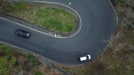 Serpentine-road-and-passing-cars,-ascending-top-down-aerial-drone-view-of-turn-curve
