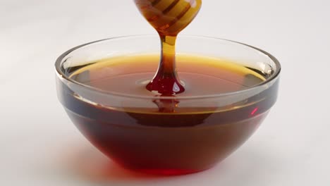 Stirring-honey-in-bowl-with-honey-stick-dipper-and-drizzling-dripping-in-slow-motion-with-white-background-in-4k