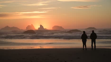 Silhouetted-couple-watches-colorful-sunset-in-Bandon-Beach,-Oregon-Coast,-USA