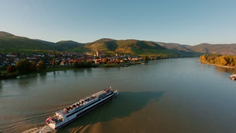 Ascending-fpv-shot-of-a-danube-boat-passing-weissenkirchen-town-in-the-wachau-valley