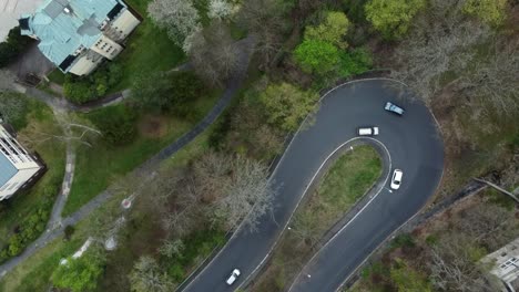Aerial-drone-view-of-serpentine-or-curvy-road-with-driving-cars-passing-by,-top-down-rotating-shot