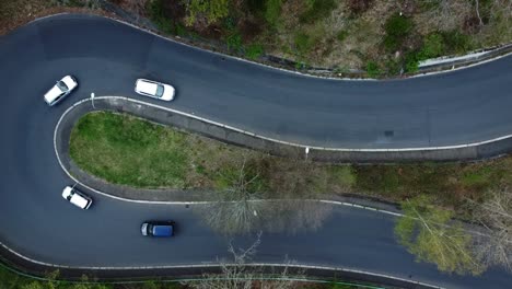Top-down-ascending-drone-view-of-cars-driving-and-passing-serpentine-or-curvy-road