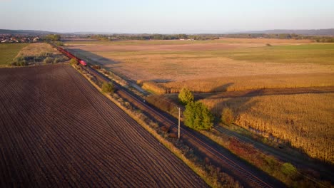 Train-passing-by-factory-with-cargo-on-farm-fields-in-the-sunset