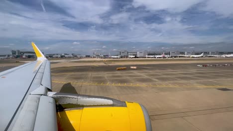 View-of-yellow-airplane-wing-and-engine-moving-on-ground-in-London-Gatwick-British-airport-in-UK