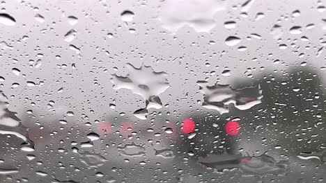 Nahaufnahme-Von-Regnerischem,-Depressivem-Wetter-über-Der-Windschutzscheibe-Und-Roten-Verschwommenen-Lichtern-Des-Autoverkehrs-Im-Hintergrund-Mit-Wischer,-Der-Die-Windschutzscheibe-Von-Regentropfen-Reinigt