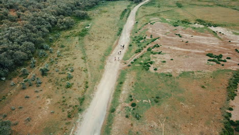 Vista-Aérea-De-Alejamiento-De-Un-Grupo-De-Ciclistas-Que-Viajan-En-Un-Camino-De-Tierra-De-Kenia