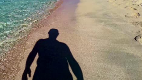 Unusual-footage-of-silhouette-shadow-of-man-walking-on-sandy-beach-seaside-turquoise-sea-water
