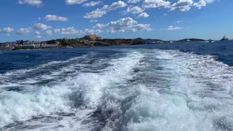 Ibiza-castle-view-from-fast-commercial-boat-ride-from-Ibiza-to-Formentera-island,-boat-moving-and-creating-waves,-public-transport-sailing,-Mediterranean-sea-fun-holiday-vacation-Spain,-4K-shot