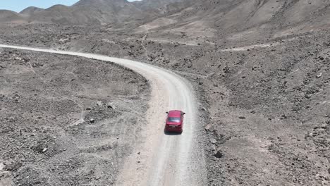 Aerial-panning-and-dolly-shot-of-a-slow-moving-red-vehicle-in-the-desert-of-peru-along-a-dusty-and-dry-desert-road-in-the-wasteland-outside-the-holy-city-of-caral-on-a-sunny-day
