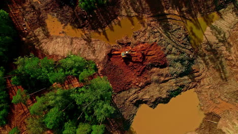 Topdown-orbit-view-of-Heavy-machinery-during-deforestation,-treetops-and-muddy-ponds-at-Development-site