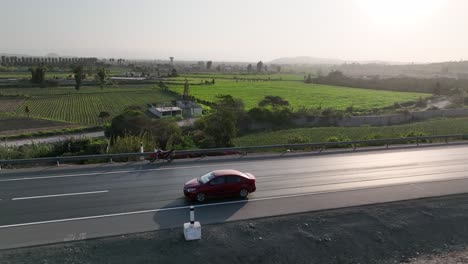 Drone-flying-over-a-moving-car-along-highway-passing-near-fields-in-Peruvian-countryside,-Side-view